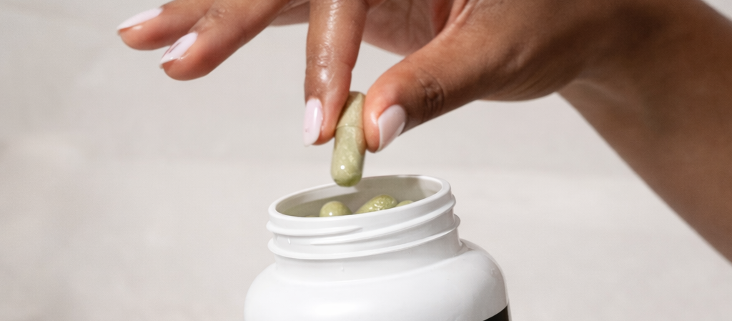 Close-up of hands holding an open M.D. Blend Allergy supplement bottle as green capsules are poured into the palm on a clean white background.